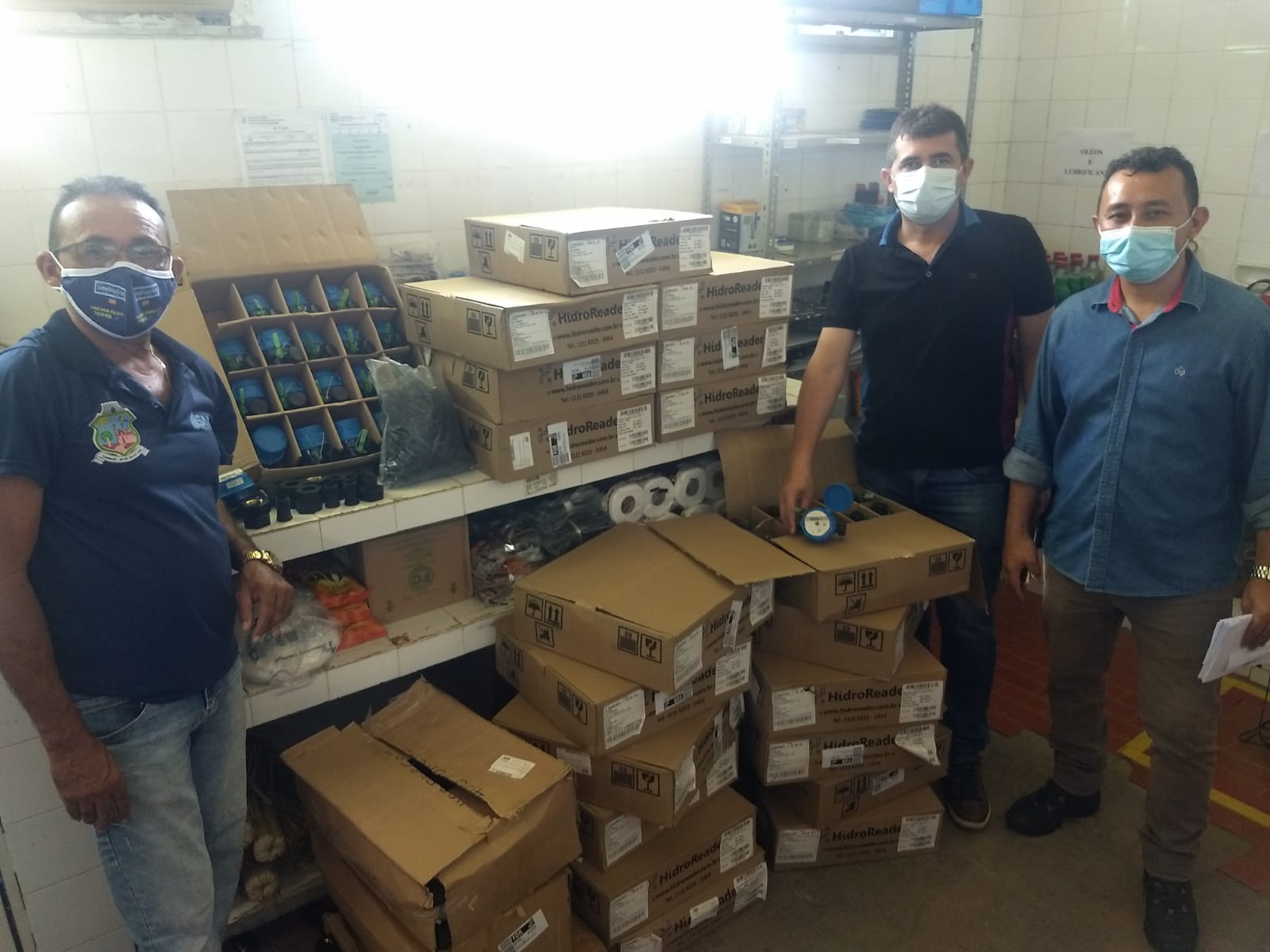 Três homens em pé ao lado de caixas