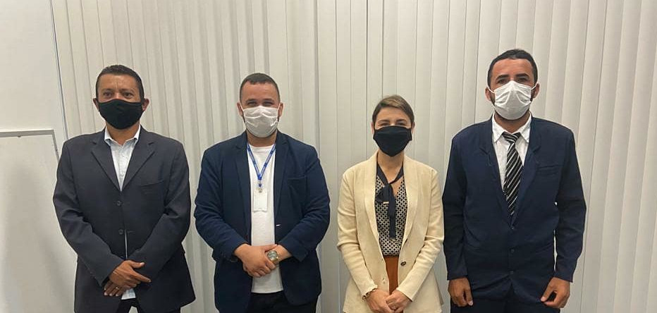 Uma mulher e três homens, lado a lado, usando máscaras, em pé, posando para foto
