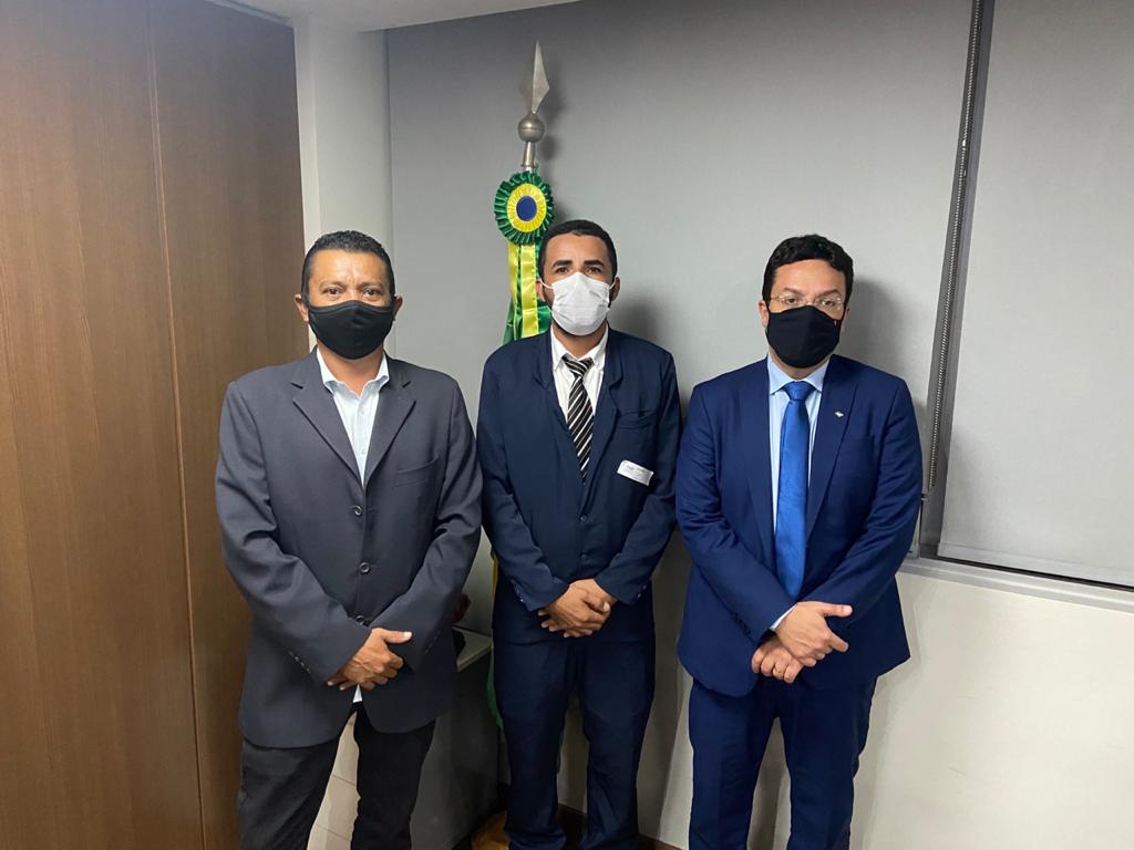 Três homens, trajando ternos e usando máscara, posando para foto