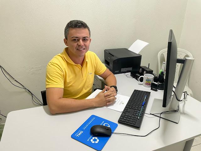 Foto de homem com uma camisa amarela de frente para um computador que está em cima de uma mesa branca