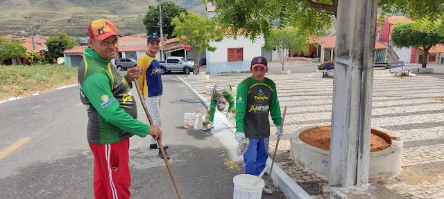 Foto de homens pintando o meio-fio na sede do município.