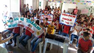 v&aacute;rias crian&ccedil;as sentadas com faixa e cartazes contra o trabalho infantil