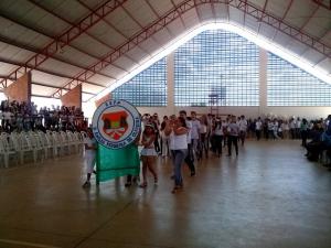 Duas pessoas segurando uma placa da Escola Em&iacute;lia Ferreira e v&aacute;rias pessoas seguindo