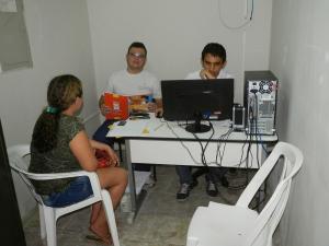  Dois homens atr&aacute;s de um bir&ocirc;, um com uma revista e o outro no computador e de fronte ao bir&ocirc; uma mulher