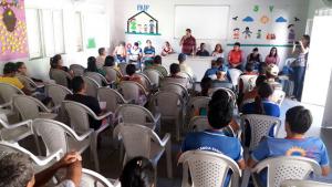 v&aacute;rias pessoas sentadas ouvindo uma pessoa falar ao microfone